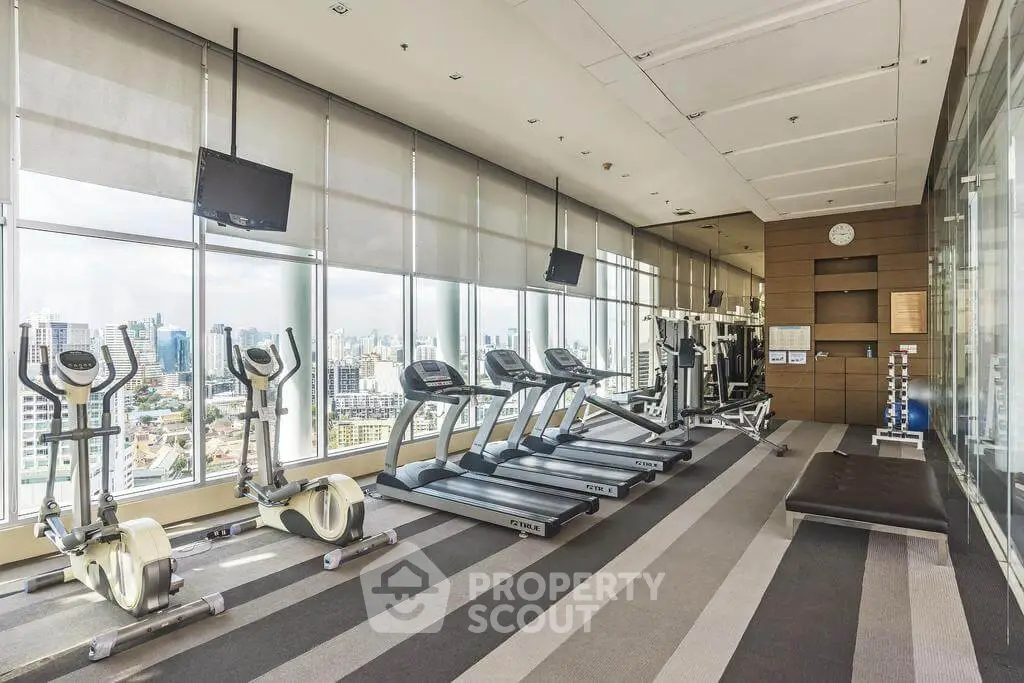 Modern gym with city view, featuring treadmills and exercise bikes in a high-rise building.