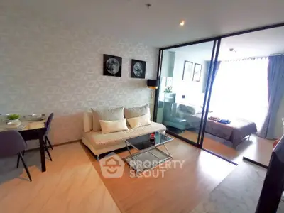 Modern living room with glass partition leading to a cozy bedroom, featuring stylish decor and ample natural light.
