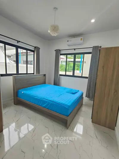 Modern bedroom with blue bedding, large windows, and sleek tile flooring in a bright, airy space.