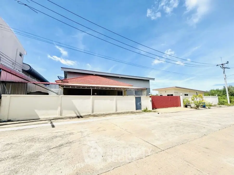 Spacious residential property with red roof and white fence under clear blue sky.