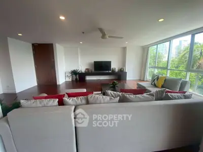 Spacious living room with modern decor and large windows offering a lush green view.