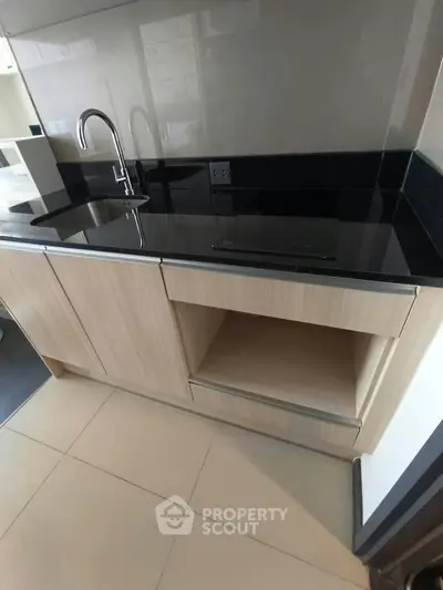 Modern kitchen with sleek black countertop and built-in sink, featuring minimalist design and ample storage.