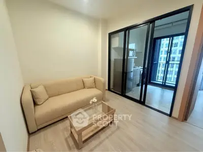 Modern living room with beige sofa and glass coffee table, adjacent to a balcony with city view.