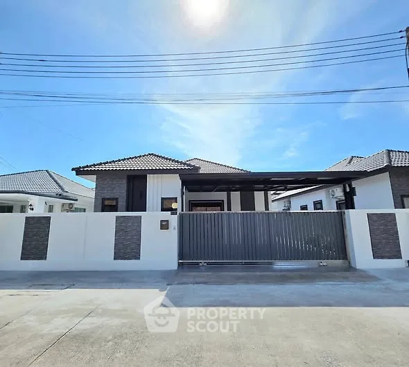 Modern single-story house with gated entrance and sleek design under clear blue sky.