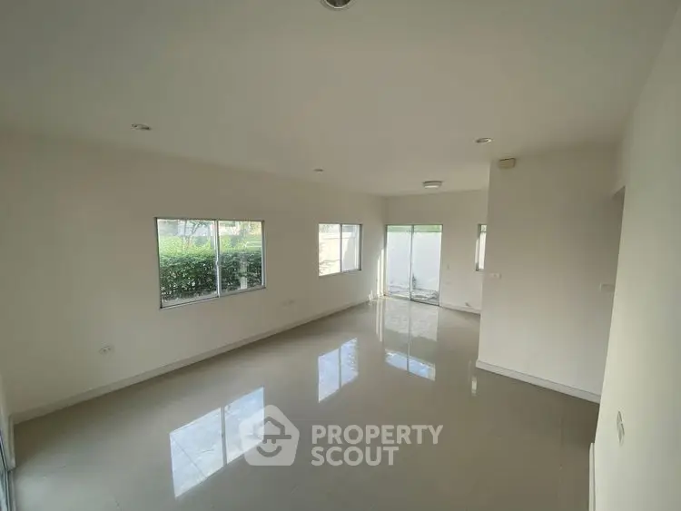 Spacious empty living room with large windows and glossy tiled floors.