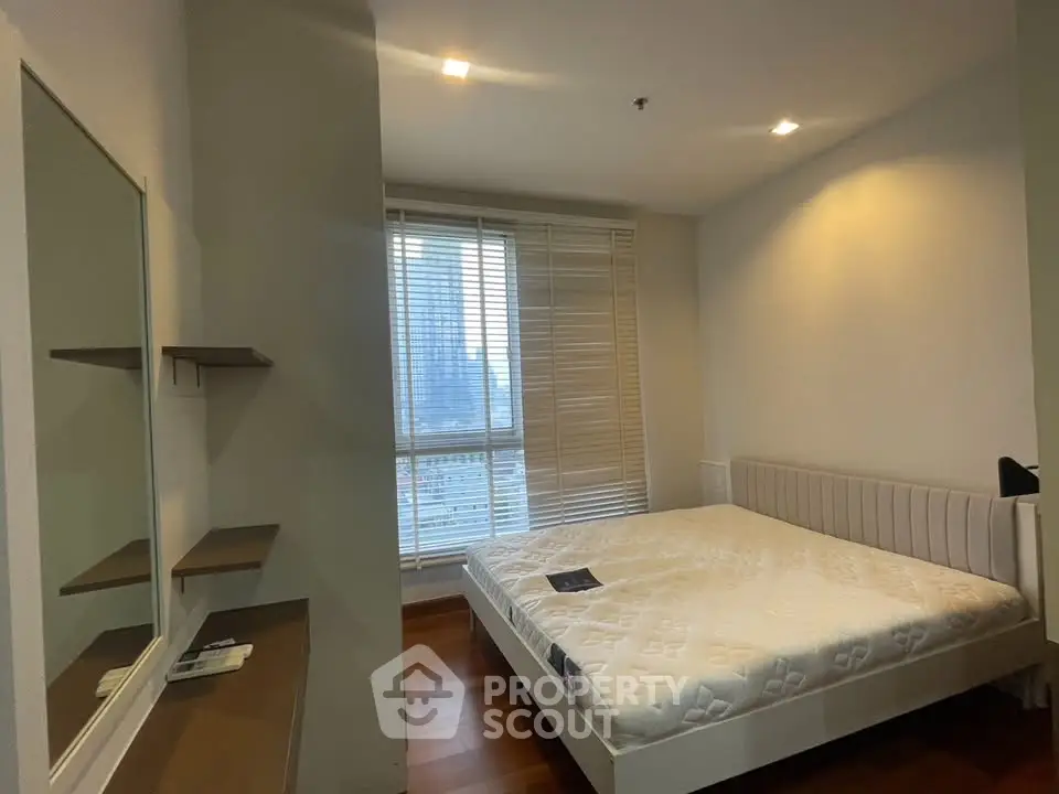 Spacious bedroom with large window and modern furnishings in urban apartment.