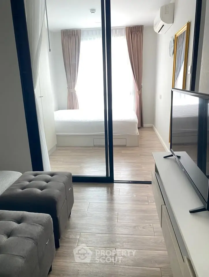 Modern apartment interior with cozy living room and bright bedroom separated by glass doors.