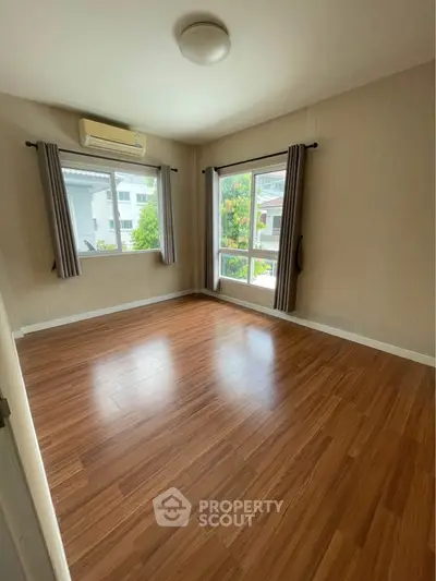 Spacious empty bedroom with wooden flooring and large windows offering natural light.