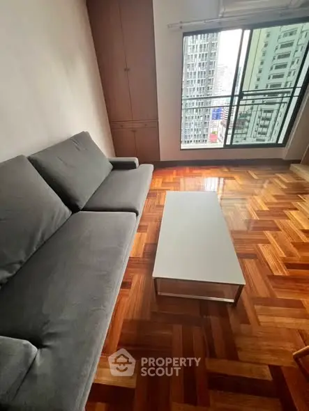 Spacious living room with parquet flooring and city view from large window.