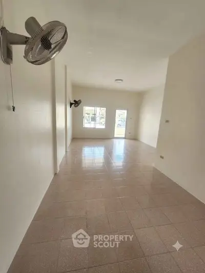 Spacious empty room with tiled flooring and wall-mounted fans, ideal for customization.