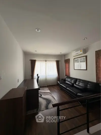 Modern living room with sleek black leather sofa, wooden flooring, and natural light from large window.