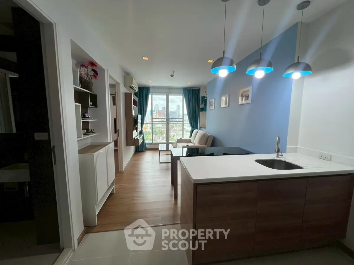Modern open-layout living room with kitchen, featuring stylish lighting and a stunning city view.
