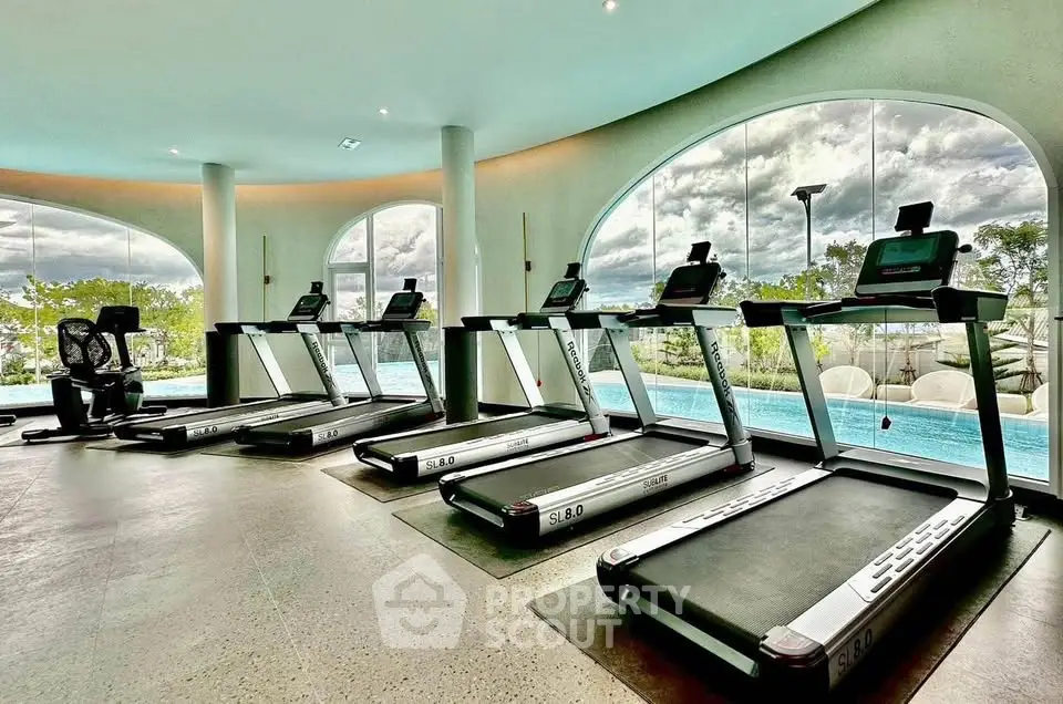 Luxurious gym with modern treadmills and pool view in upscale residential complex.