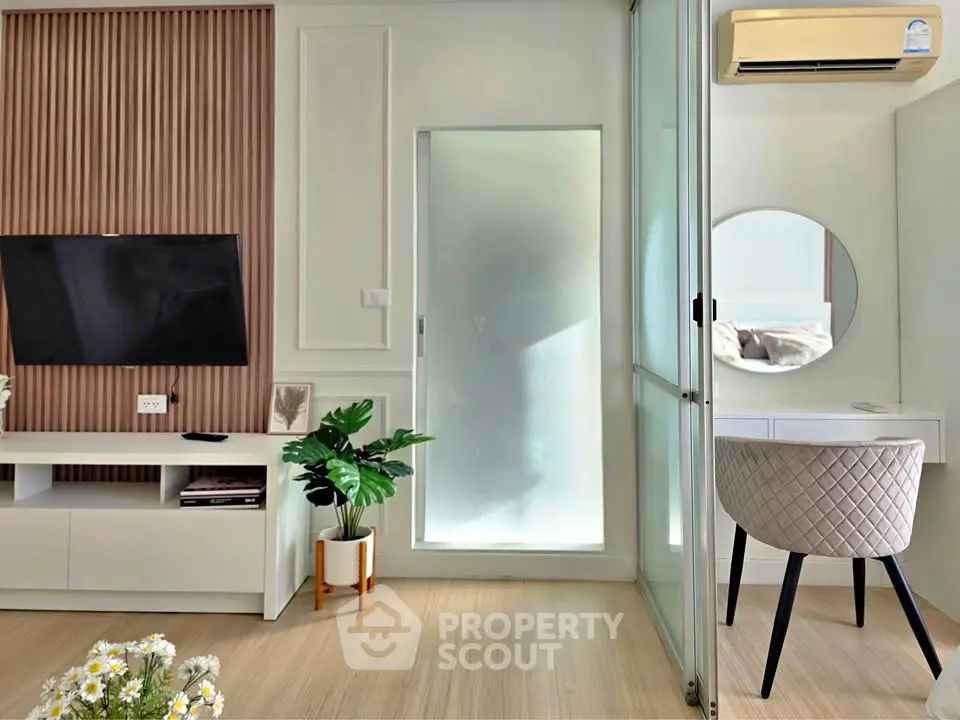 Modern living room with stylish decor, TV, and air conditioning, featuring a cozy workspace with a round mirror.