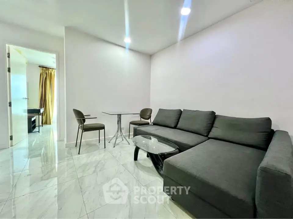 Modern living room with sleek black sofa and marble flooring, adjacent to a bright room with curtains.