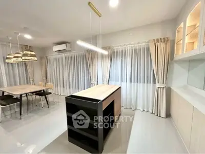 Modern open-layout kitchen with island and dining area, featuring elegant lighting and floor-to-ceiling curtains.