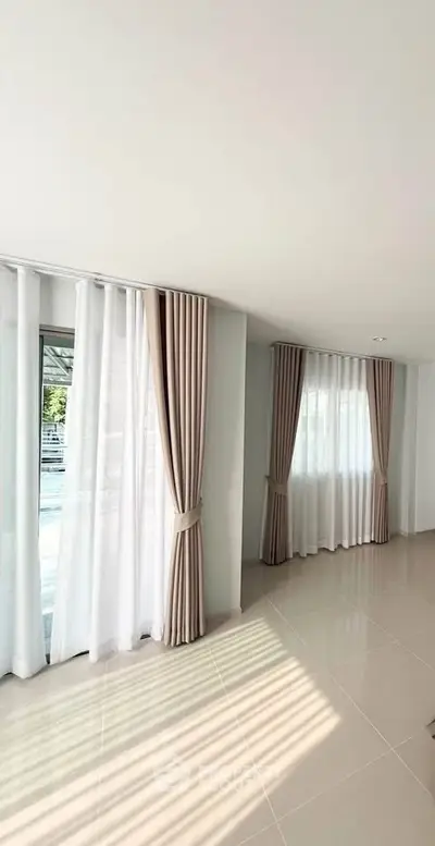 Spacious living room with large windows and elegant curtains, offering abundant natural light and a serene atmosphere.