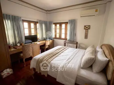 Cozy bedroom with elegant decor, featuring a comfortable bed, wooden furniture, and ample natural light.