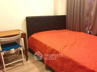 Cozy bedroom with vibrant orange bedspread and compact workspace.