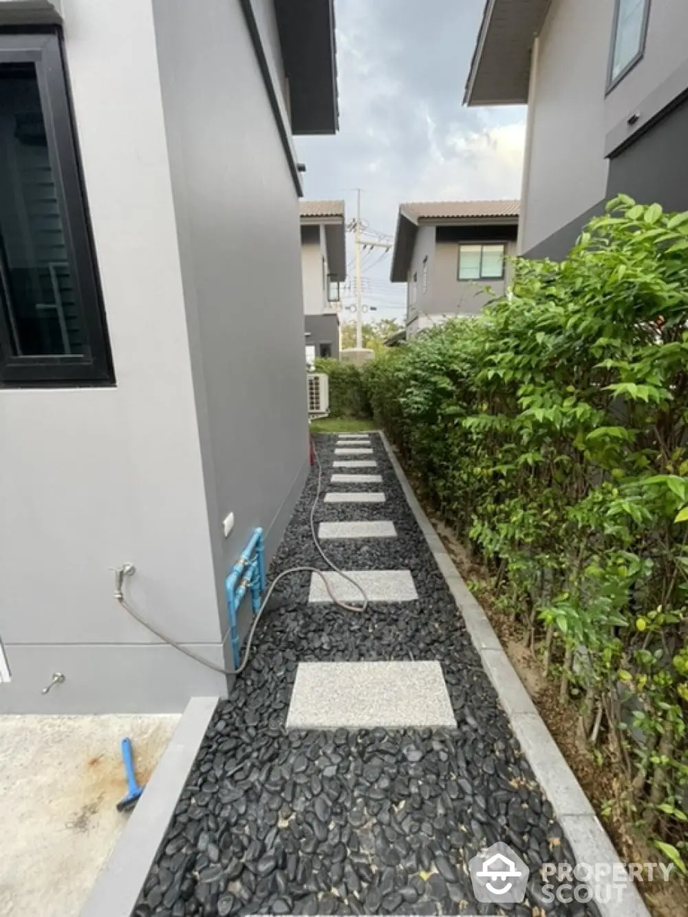 Serene pathway between modern homes with decorative stones and lush greenery, perfect for peaceful suburban living.