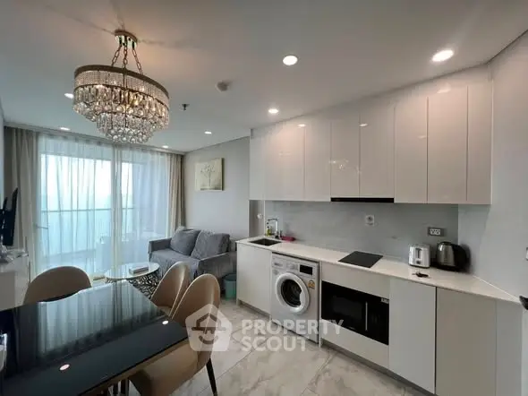 Modern open-plan living room and kitchen with elegant chandelier and balcony view.