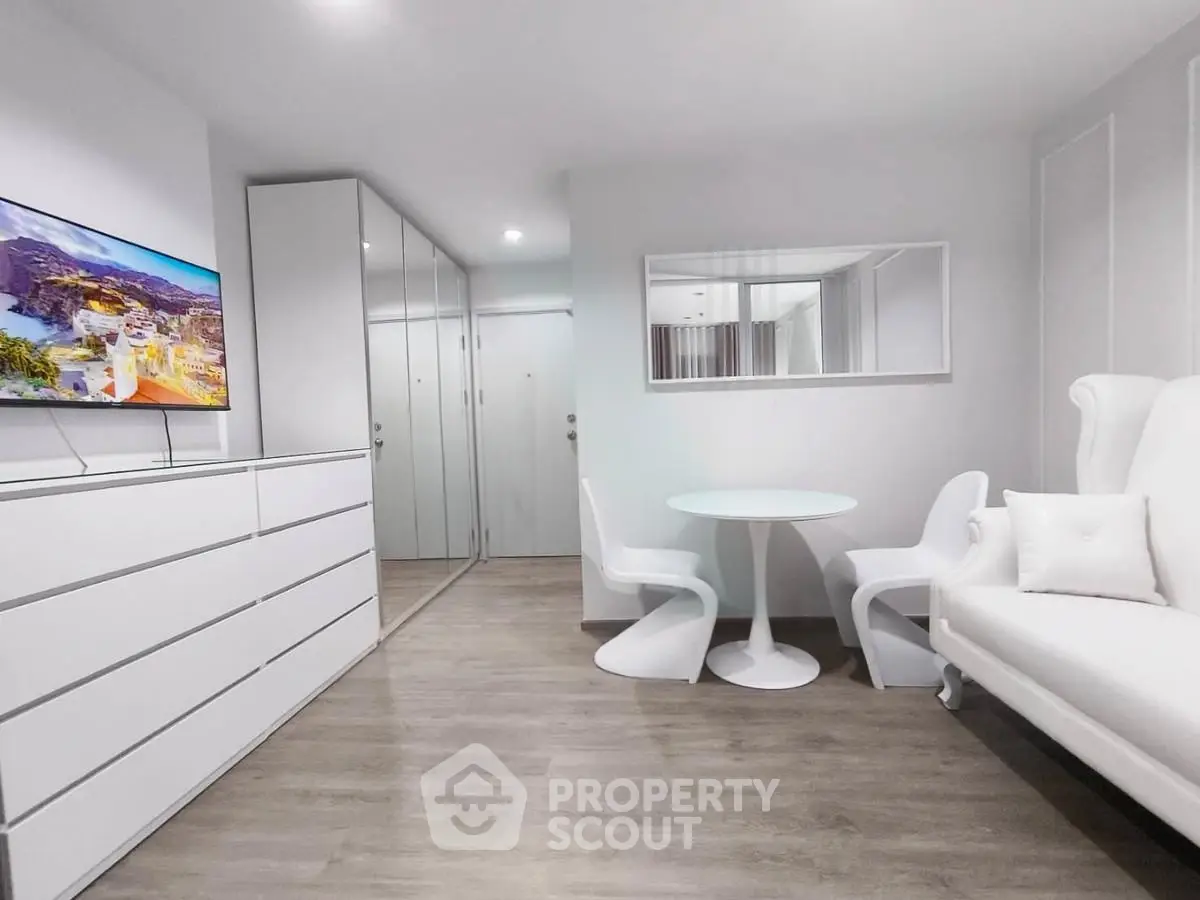 Modern minimalist living room with sleek white furniture and mirrored closet doors.
