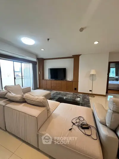 Spacious living room with modern beige sofa and large TV, featuring a balcony view.
