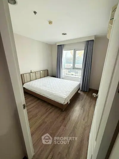 Cozy bedroom with wooden flooring and large window for natural light