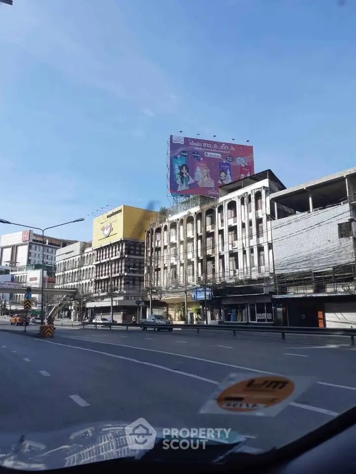 Urban street view with commercial buildings and large billboard under clear blue sky.