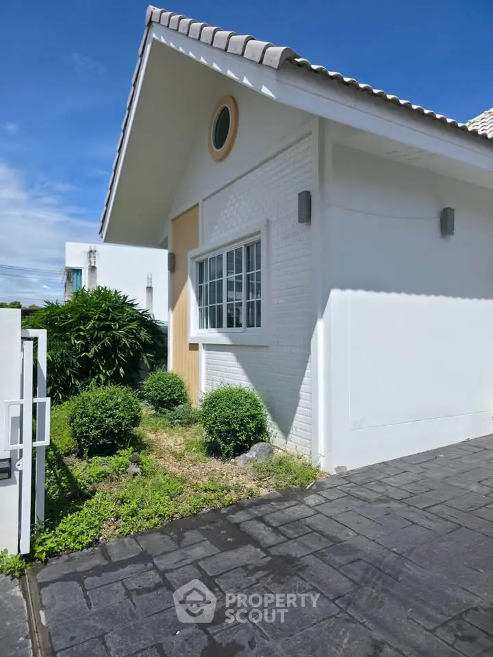Charming white house exterior with lush greenery and modern design under a clear blue sky.