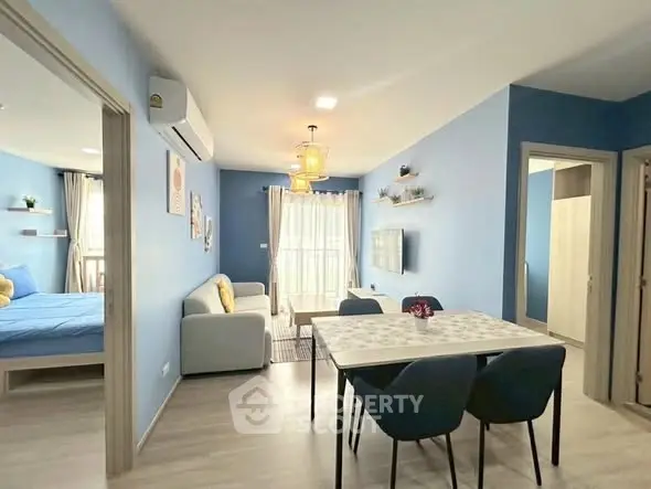 Modern open-plan living room with dining area and view into a cozy bedroom, featuring stylish decor and ample natural light.