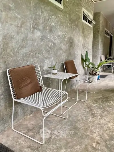 Chic outdoor patio with modern white metal chairs and lush potted plants on concrete flooring.