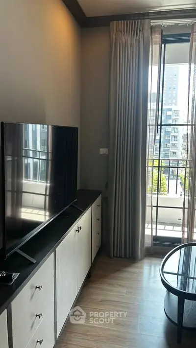 Modern living room with sleek TV setup and balcony view in urban apartment.