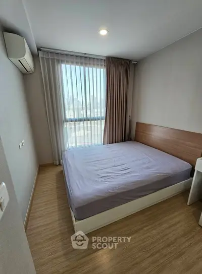 Cozy bedroom with large window and modern furnishings, perfect for urban living.