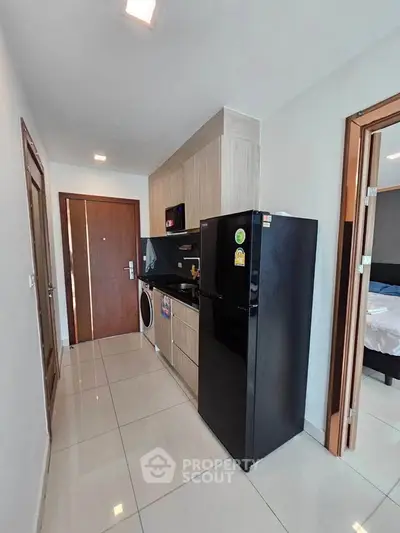 Modern apartment kitchen with sleek black fridge and washing machine, adjacent to cozy bedroom.