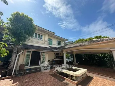 Charming two-story house with spacious driveway and lush greenery under a clear blue sky.