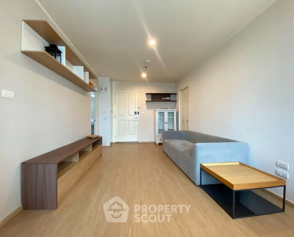 Spacious and modern living room with sleek wooden flooring, minimalist furniture, and a well-equipped open kitchen layout.
