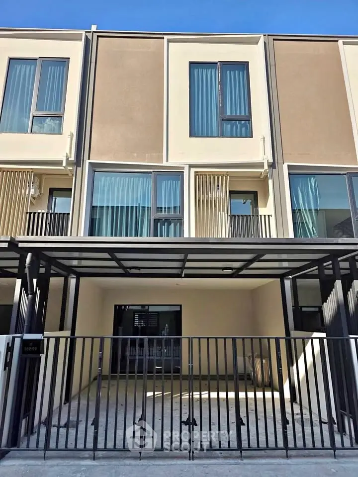 Modern townhouse exterior with sleek design and large windows, featuring a gated entrance and covered parking area.