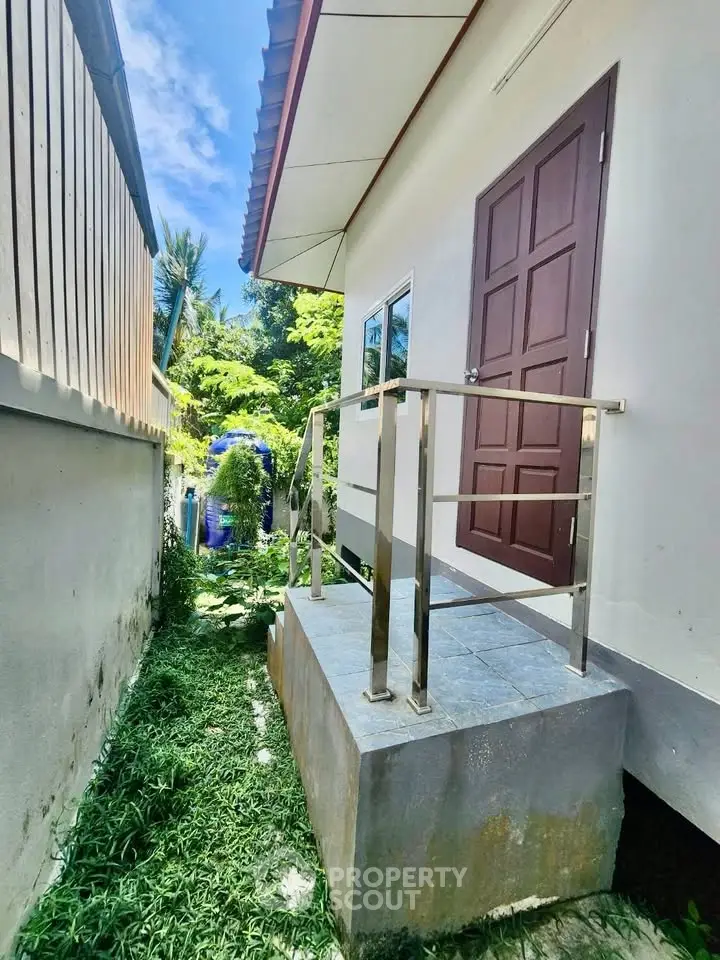 Charming exterior view of a modern home with a small elevated entrance and lush greenery.