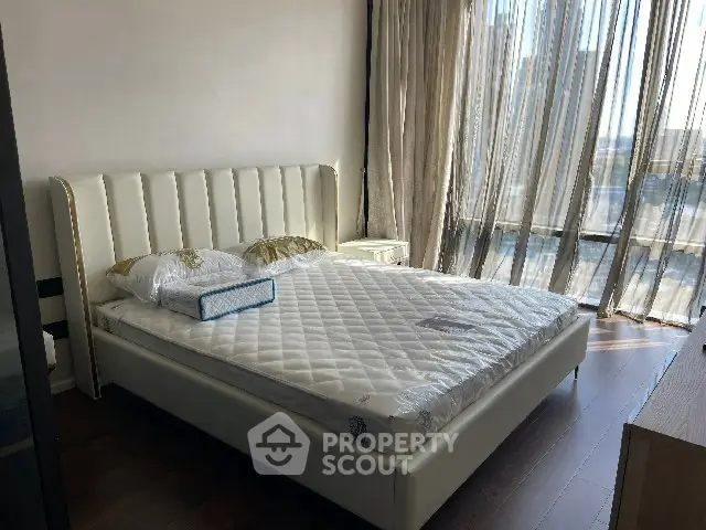 Modern bedroom with elegant bed and floor-to-ceiling windows offering natural light.