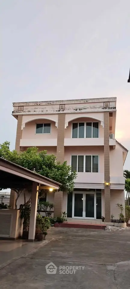 Elegant three-story residential building with modern facade and lush greenery in the front yard.
