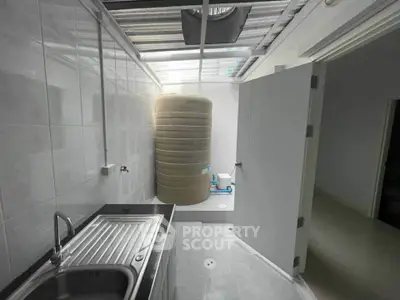 Compact utility room with stainless steel sink and large water tank