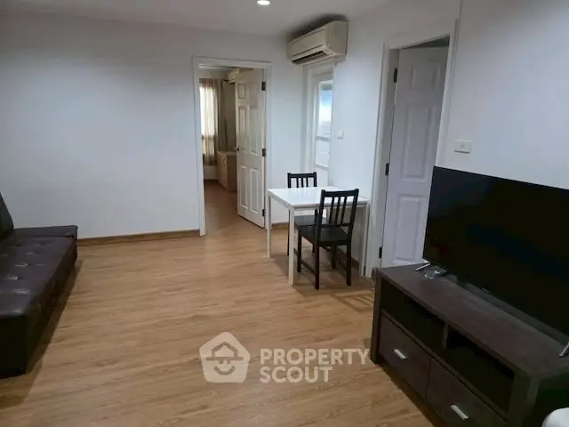 Modern living room with wooden flooring, TV, and dining area in cozy apartment.