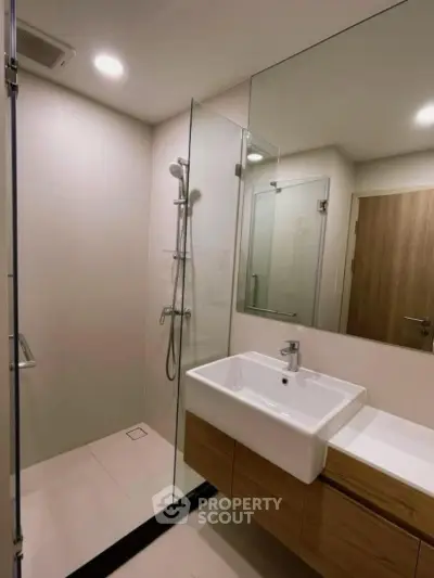 Modern bathroom with glass shower and sleek vanity in contemporary apartment.