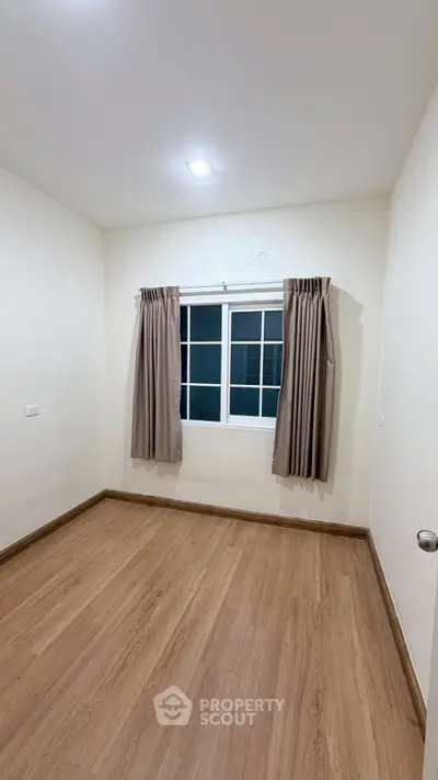 Spacious empty room with wooden flooring and large window, perfect for customization.