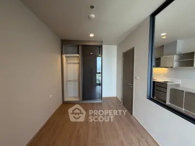 Modern apartment interior with wooden flooring and built-in wardrobe, featuring a view into a sleek kitchen area.
