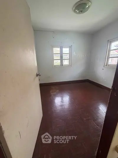 Spacious empty room with wooden flooring and natural light from two windows.