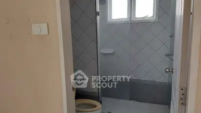Compact bathroom with tiled walls and glass shower enclosure, featuring a small window for natural light.