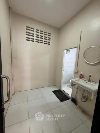 Compact bathroom with minimalist design and white tiles, featuring a wall-mounted sink and round mirror.