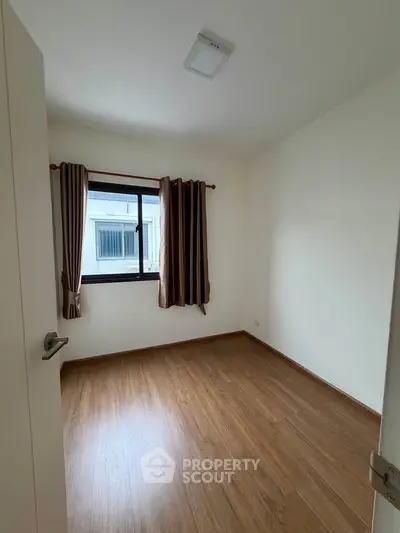Spacious empty bedroom with wooden flooring and large window